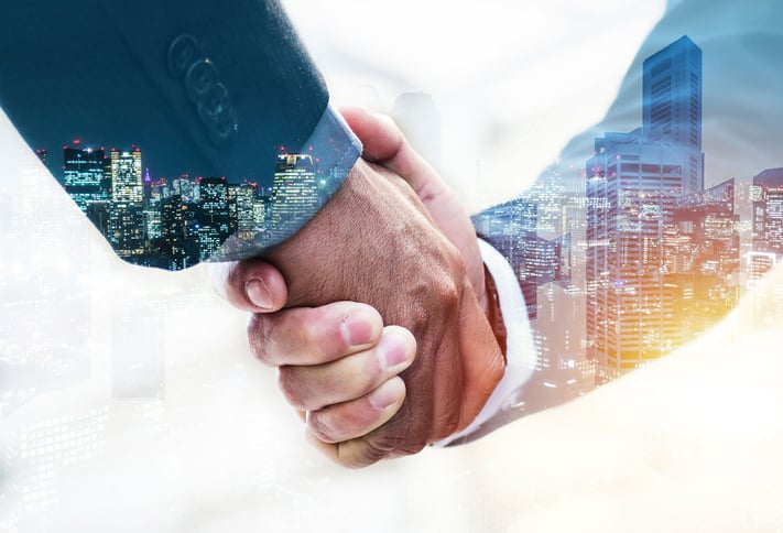 two male hands shaking with dark colored suites and white under shirts