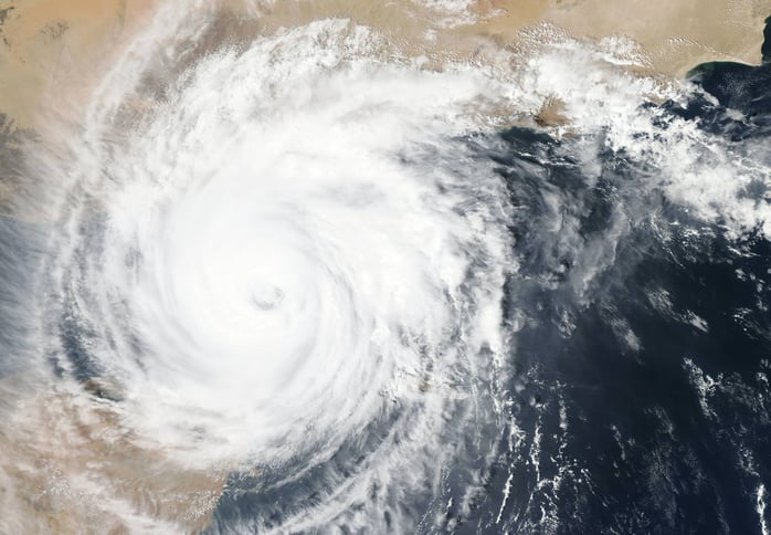 A hurricane as seen from space - a white vortex of clouds crashing against pale beige coastline.